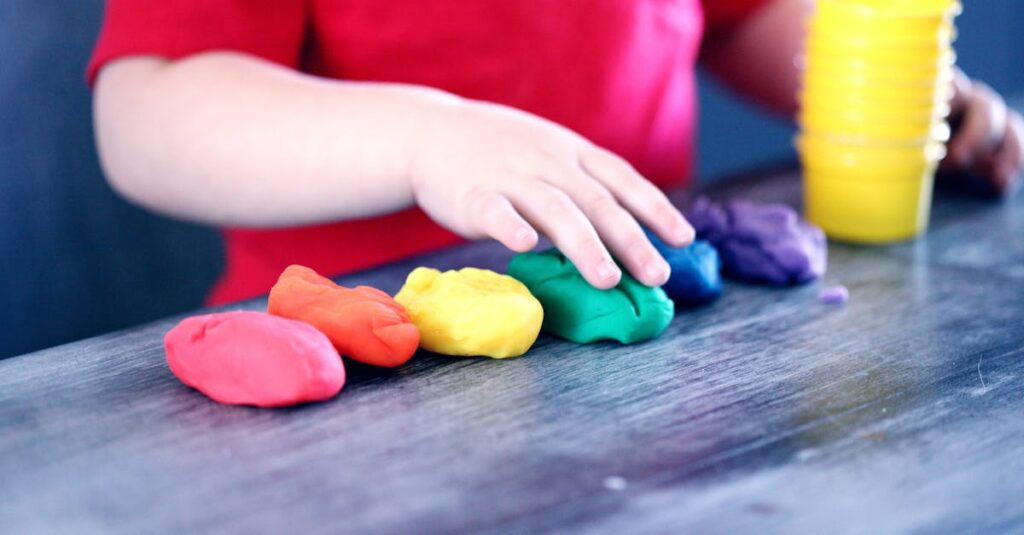 A young child with rainbow-colored modeling clay and stacking cups on a table indoors.