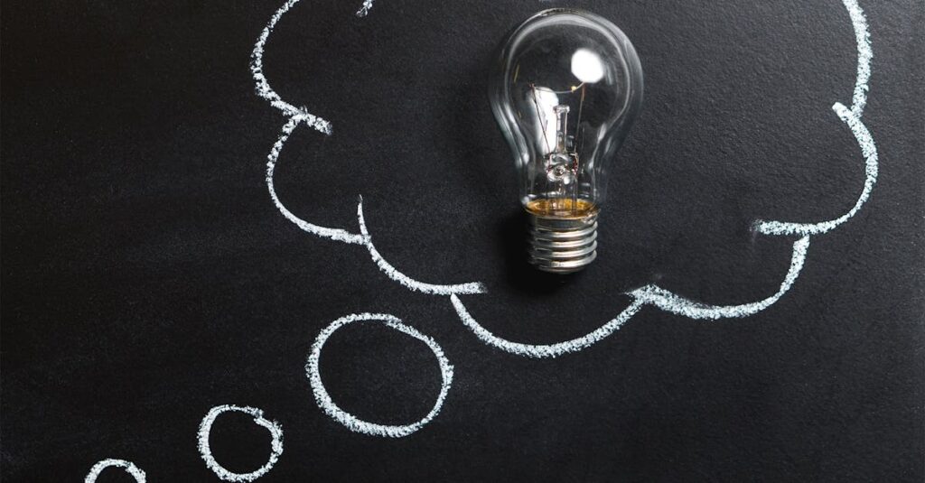 Light bulb laying on chalkboard with drawn thought bubble, symbolizing creative ideas.