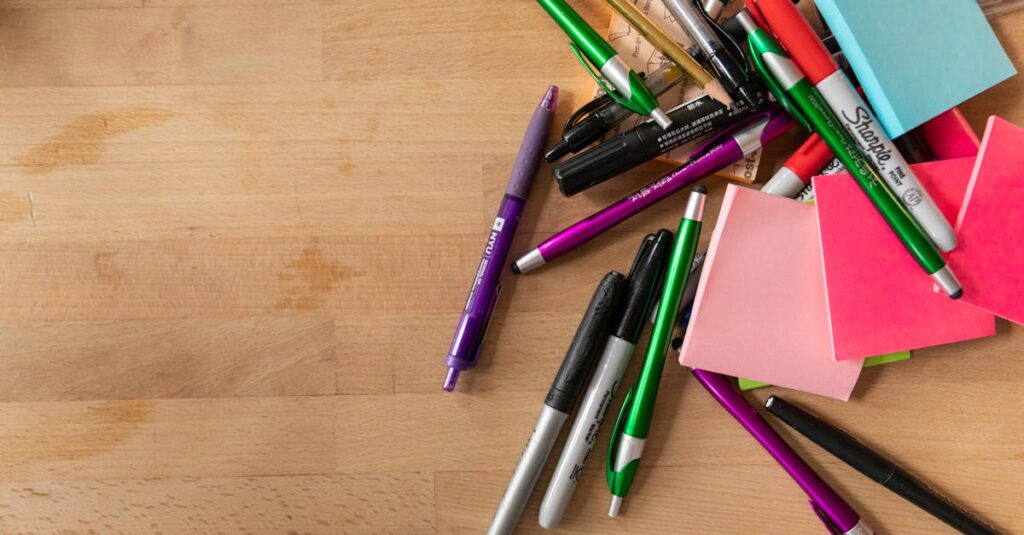 A variety of pens, markers, and sticky notes scattered on a wooden desk.